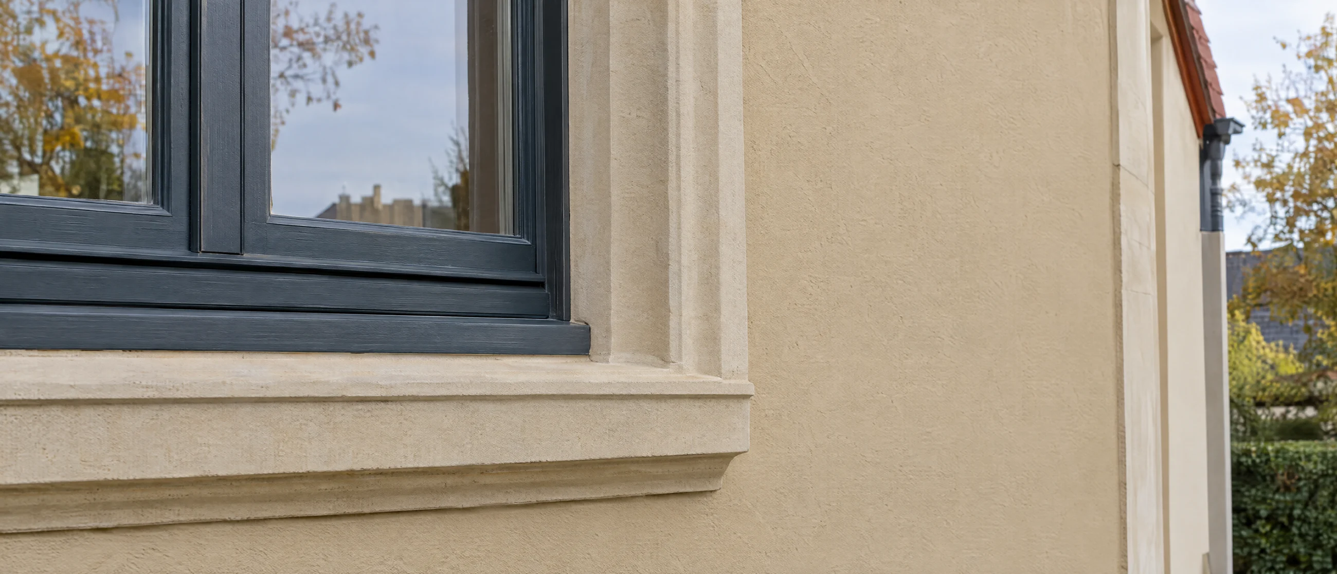 Anthrazitfarbenes Fenster in einer hellen Putzfassade mit Sandsteingewände