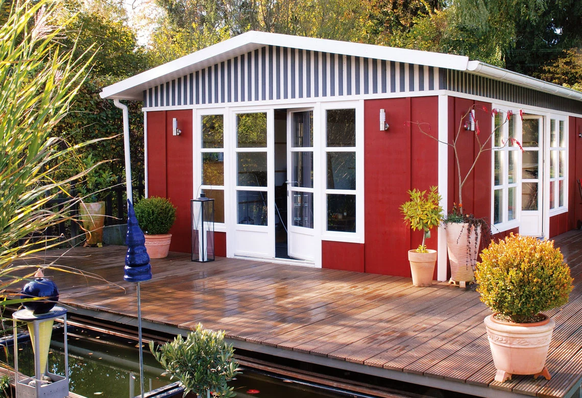 Rot-weißes Gartenhaus mit Holzterrasse am Teich